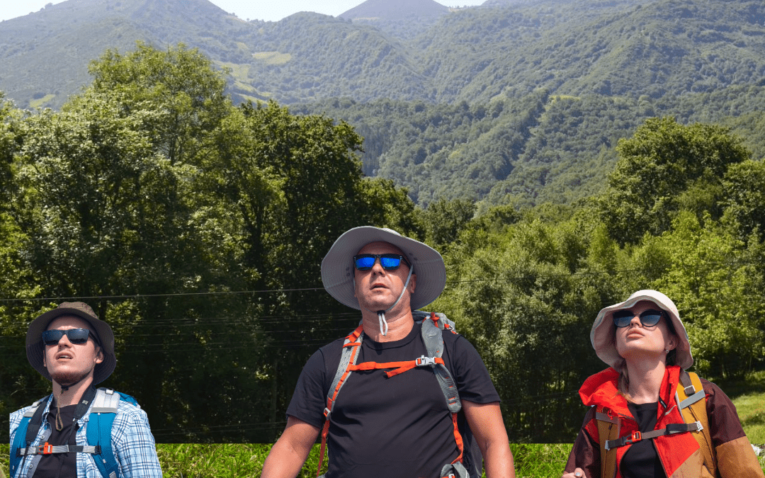 Tres peregrinos con mochilas y bastones de senderismo avanzan por un paisaje montañoso y verde en la cuarta etapa del Camino de Oviedo a Covadonga, desde la Cruz de Bendición hasta el Alto de Espinadal, con la sierra asturiana al fondo bajo cielo despejado.
